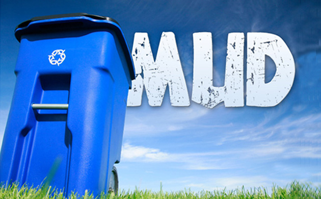 La foto rappresenta un cassonetto della spazzatura con scritta MUD su erba e cielo azzurro